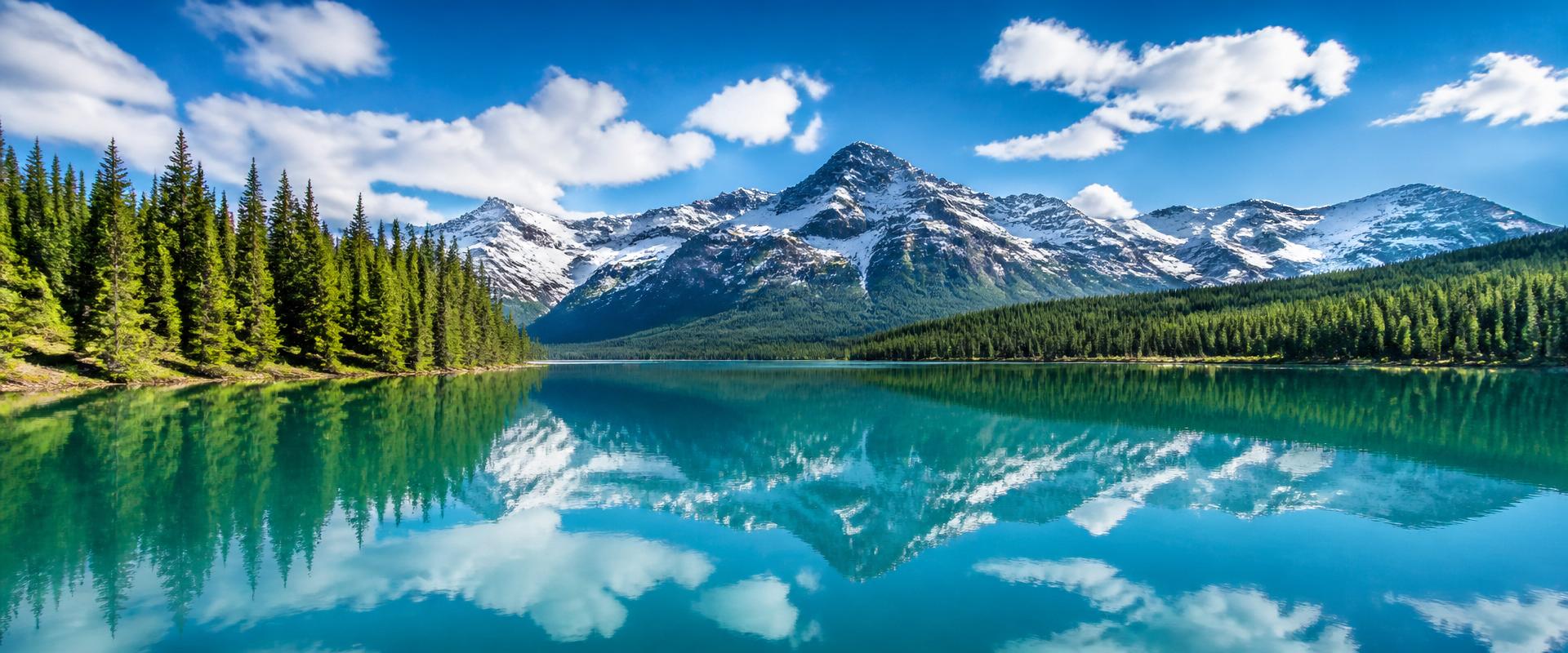 Bright turquoise Montana mountain lake surrounded by pine forest and snow-capped peaks
